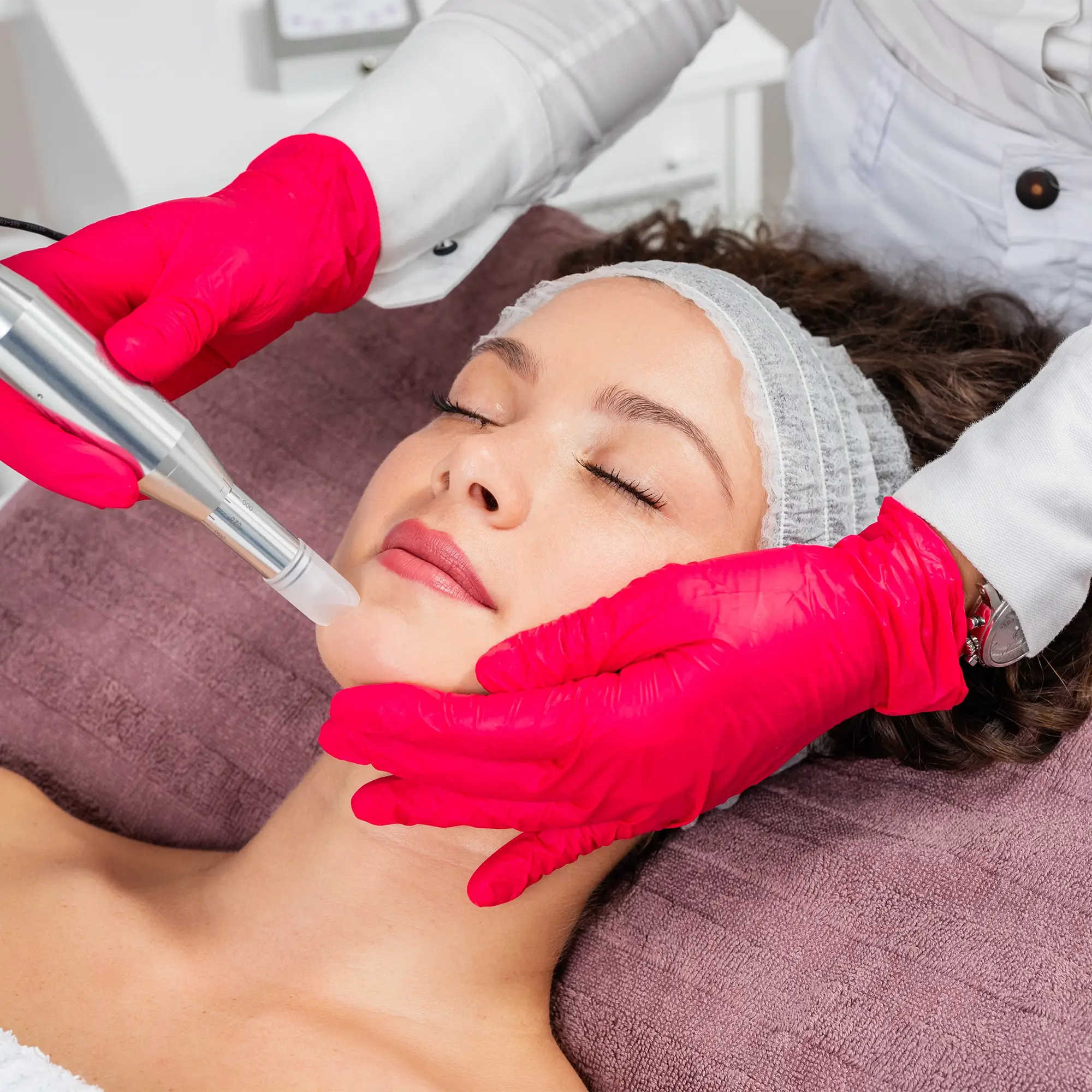 Clinician wearing pink gloves using microneedling pen along patient’s cheek and jawline 