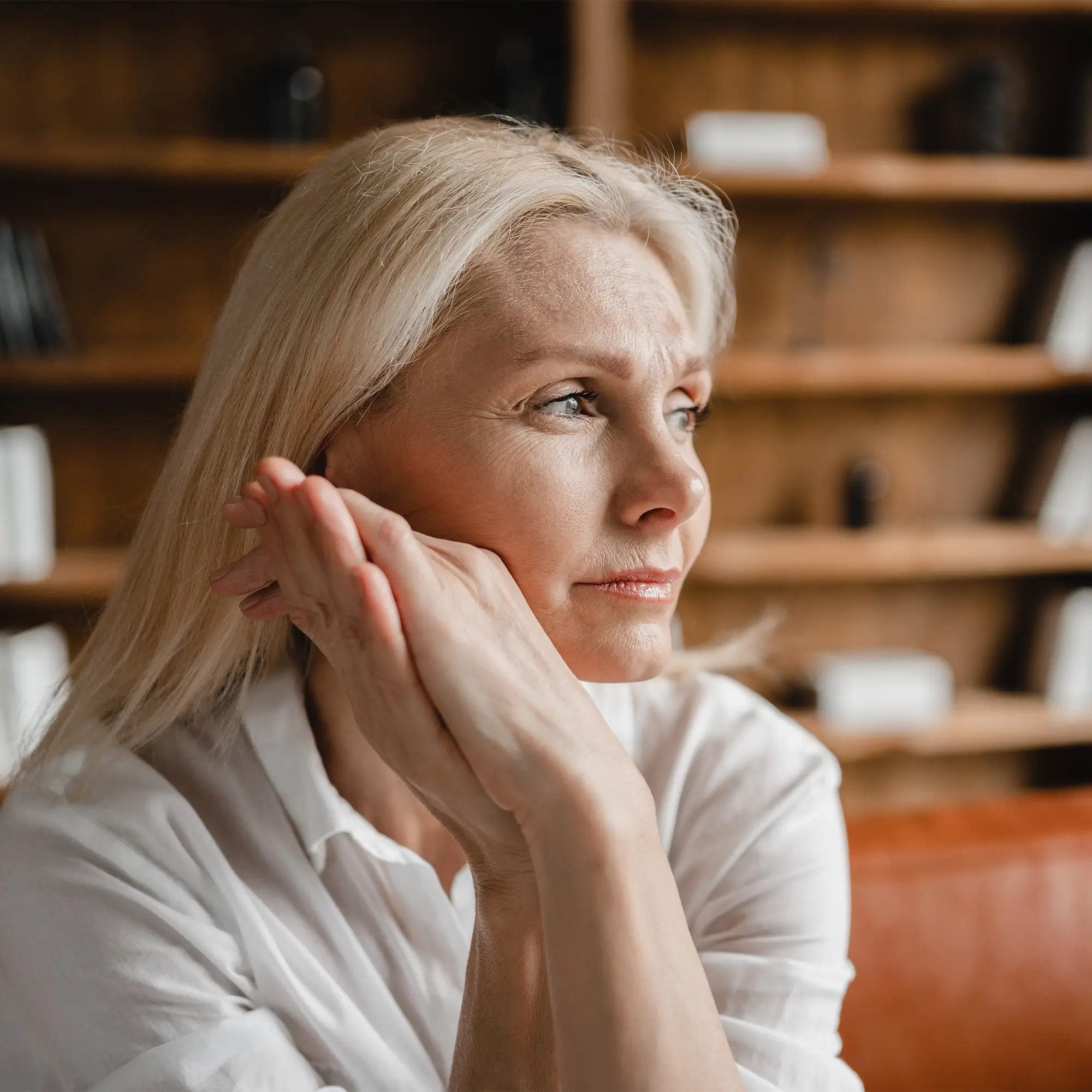 Middle aged woman sitting at table with hand on forehead due to hot flashes and mood changes 