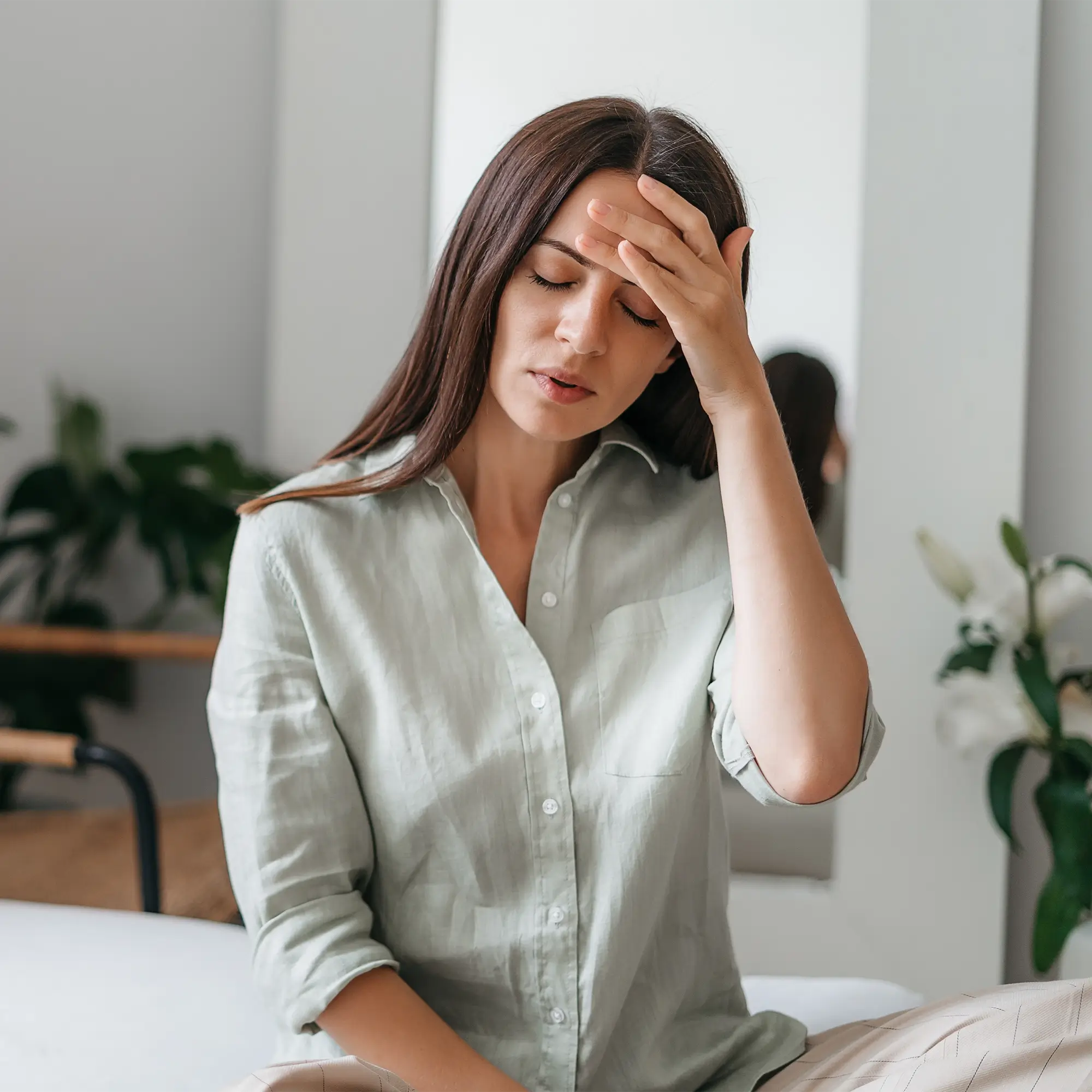Woman in dark room holding the side of her head with intense migraine pain 